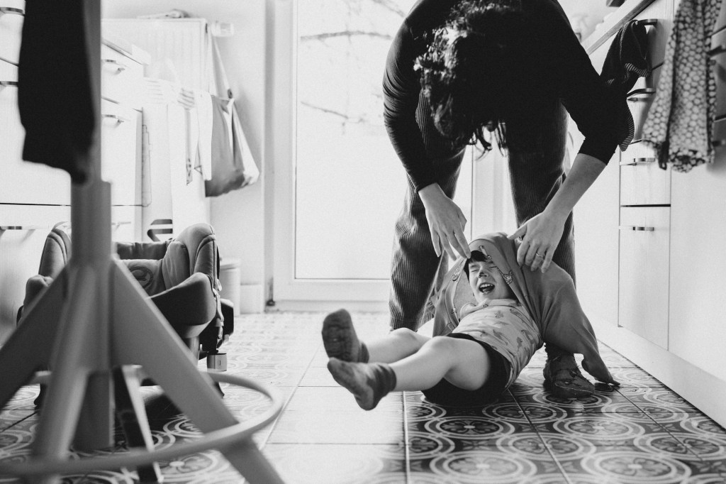 Lachendes Kleinkind während Mama versucht es anzuziehen