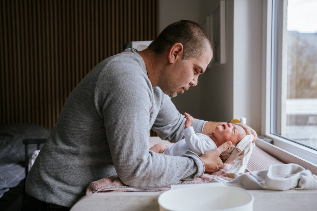 Vater zieht Neugeborenes um im Wochenbett