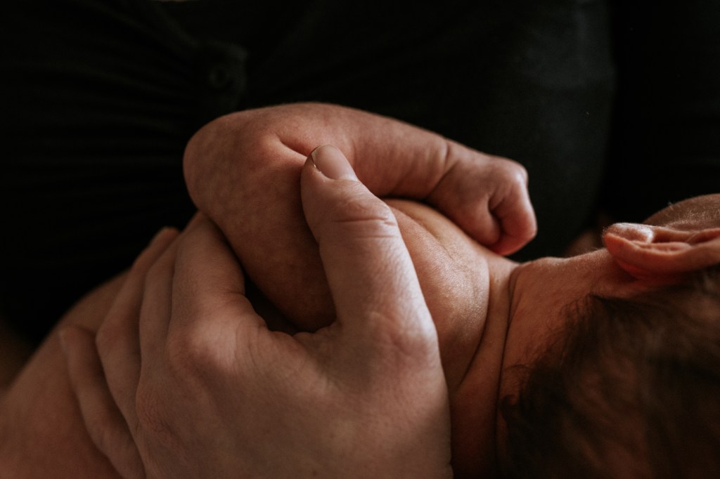 Nahaufnahme von einer Mama die ihr Neugeborenes in den Händen hält
