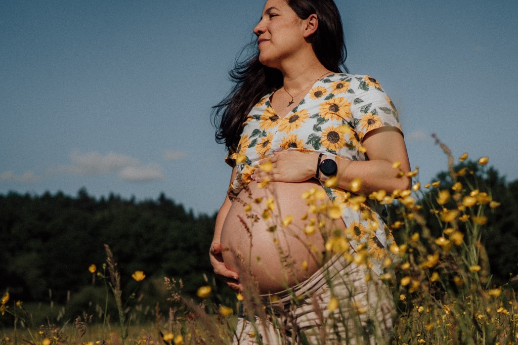 Schwangere Frau im Butterblumenfeld blickt zur Seite