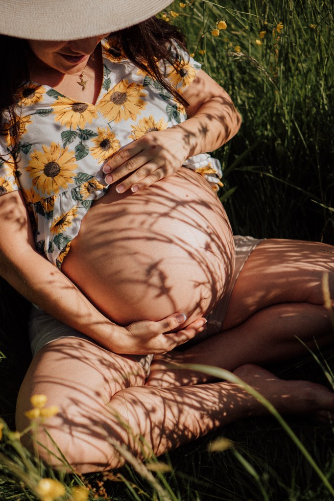 Schwangere Frau sitzt im Gras