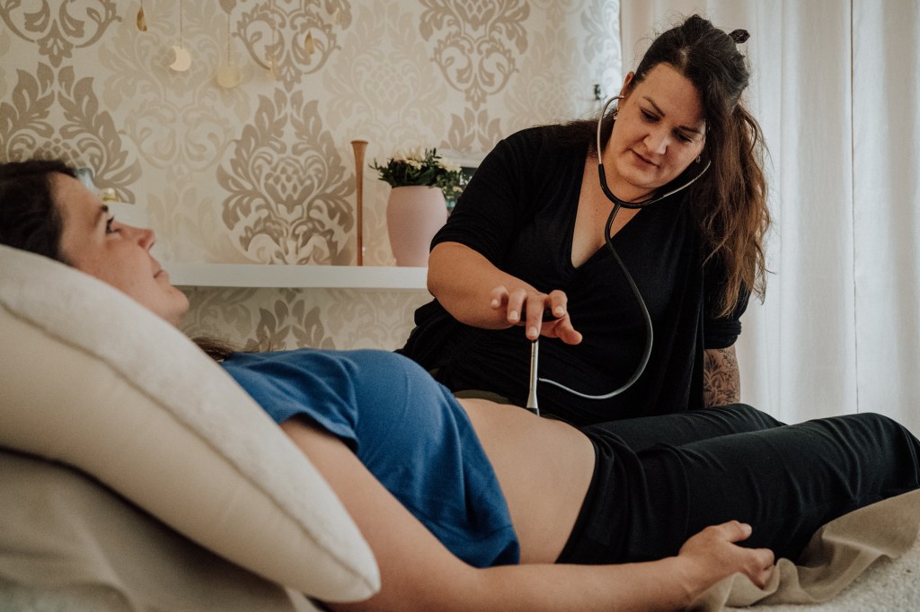 Hebamme hört während einer Vorsorge die Herztöne des Babys im Bauch ab