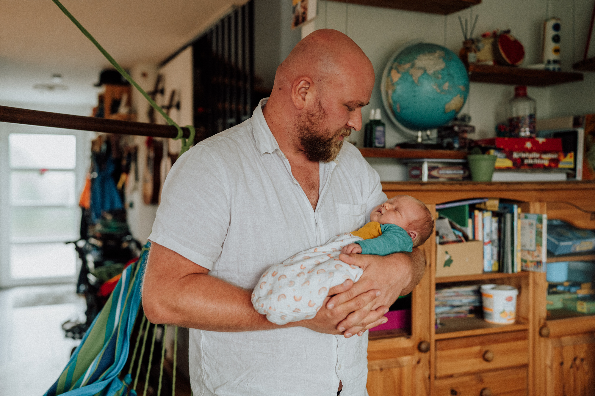 Vater hält Neugeborenes in den Armen und sieht es liebevoll an