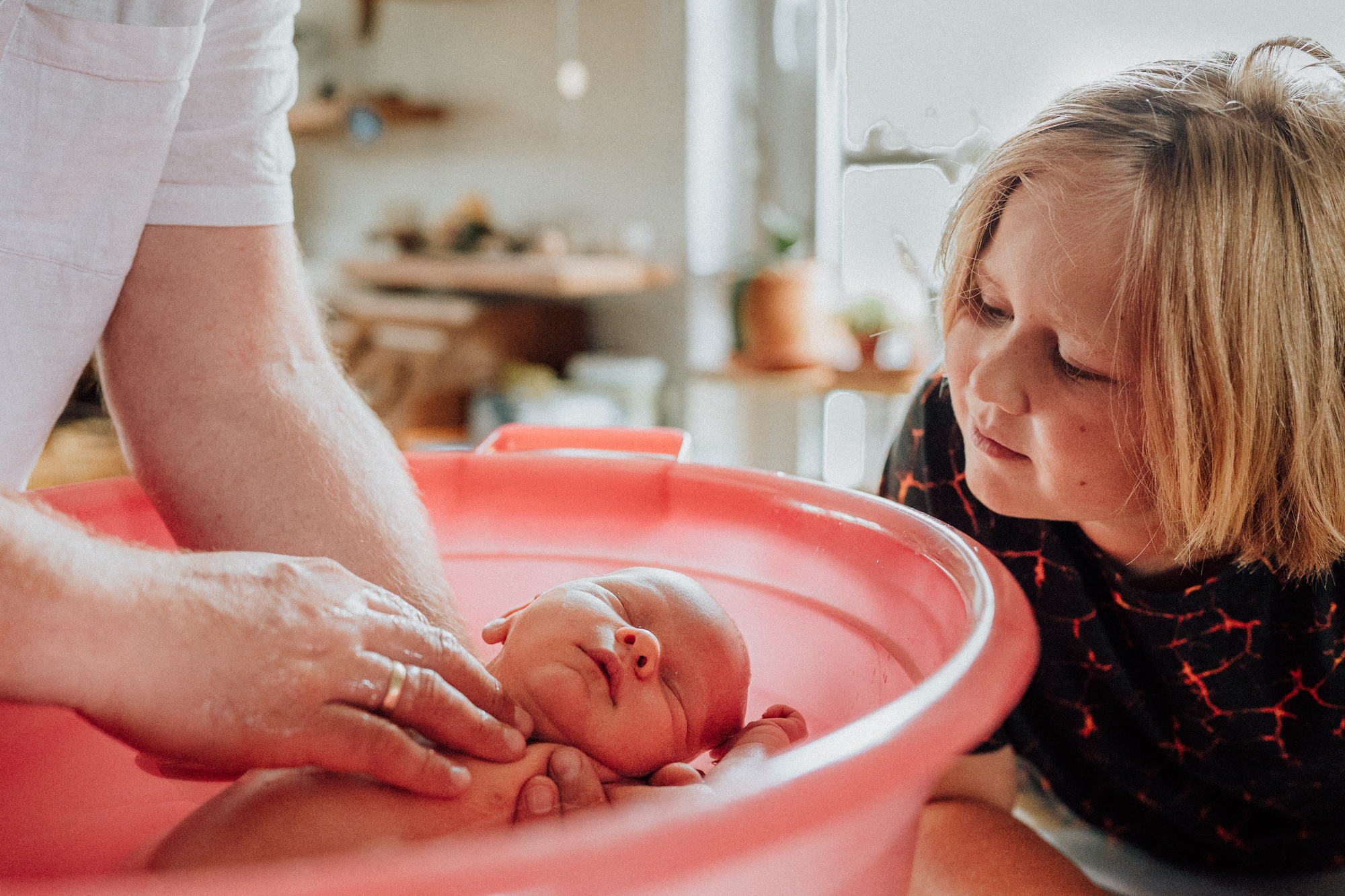 Kind schaut interessiert Baby beim baden zu