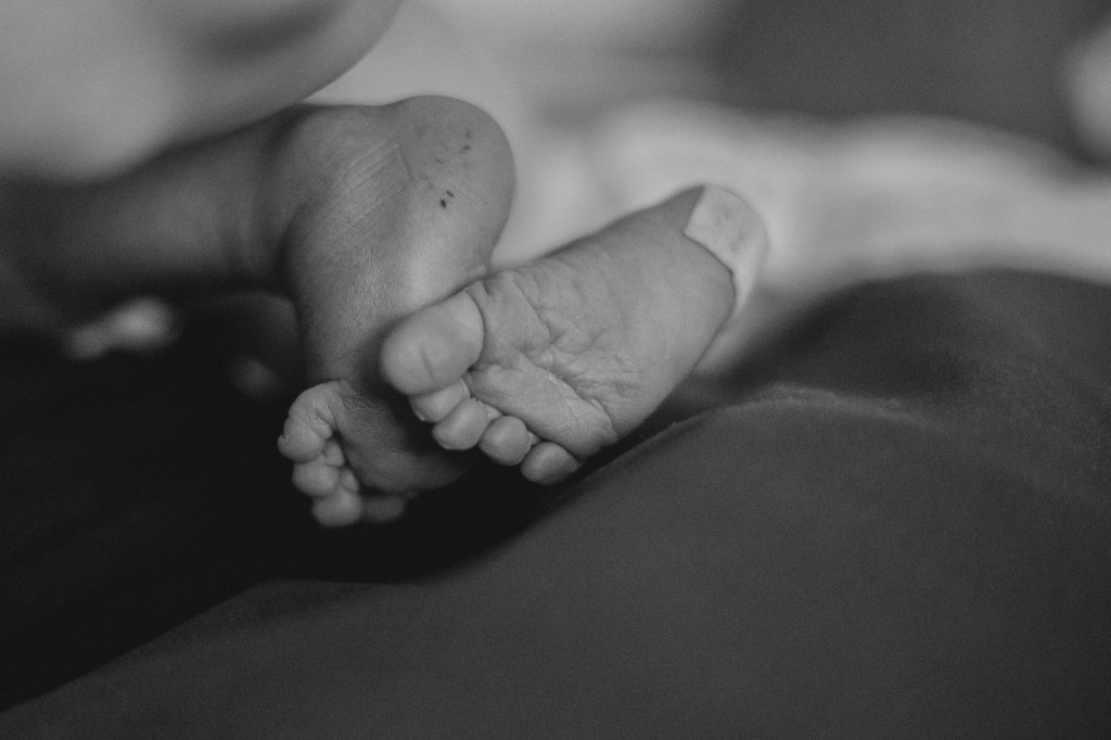 Schwarz-weiss Detailaufnahme von Babys eines Neugeborenen von unten  mit Pflaster auf der Ferse von U1