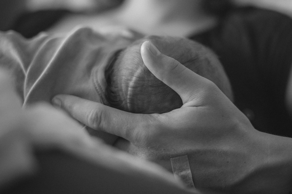 Mama hält Kopf ihres Neugeborenen